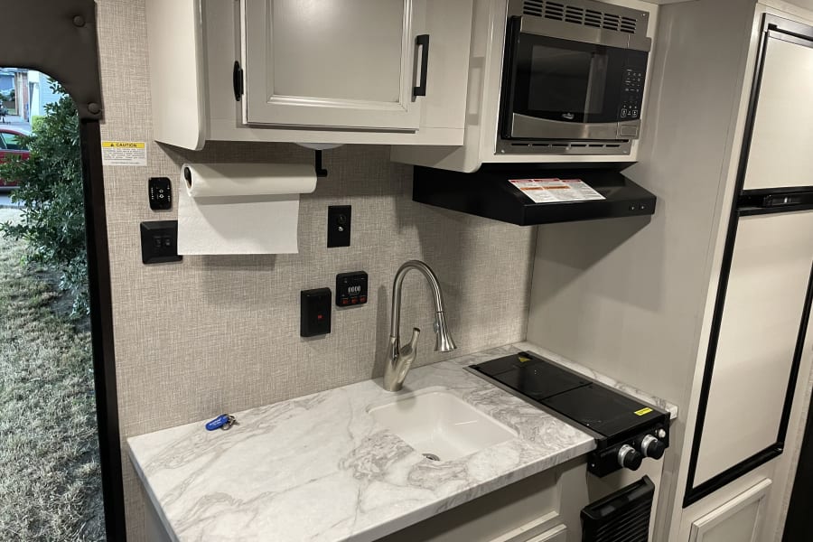 Functional RV rental kitchen with a sink, two-burner stovetop, microwave, and refrigerator for road trips.