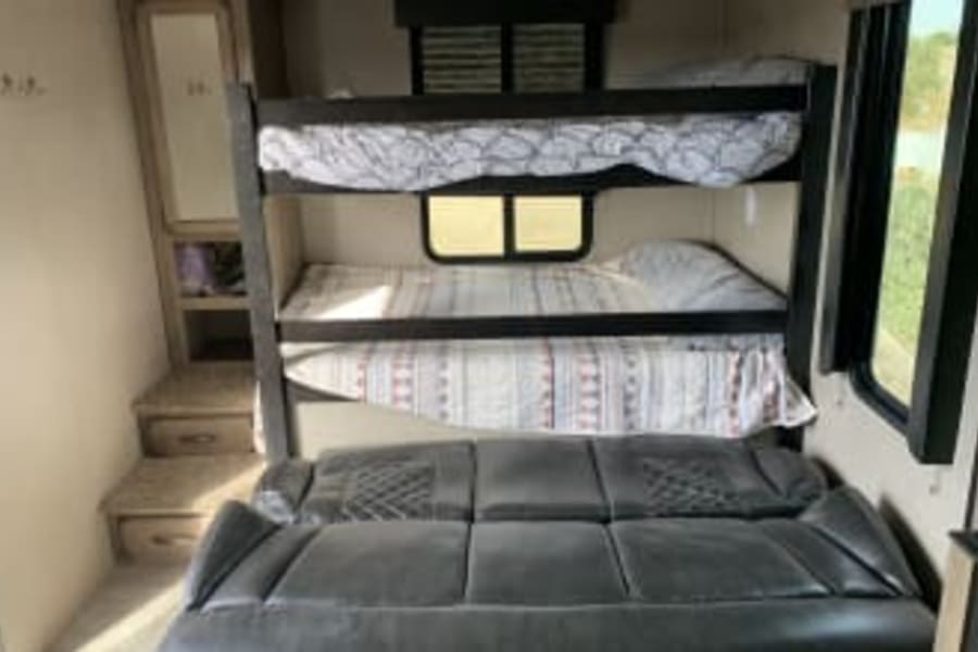 Inside an RV rental: a cozy bunk bed sleeping area over a comfortable sofa, plus built-in storage. Ideal for family trips.