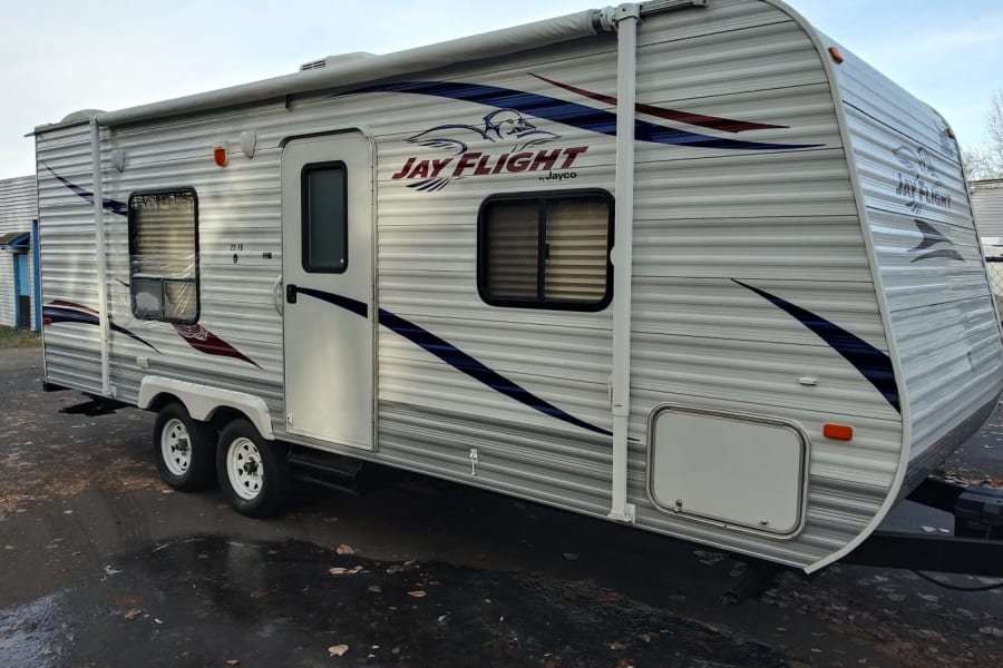 White and grey Jayco Jay Flight RV travel trailer for rv rental. Features an awning, windows, and dual axles.