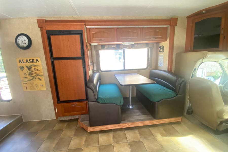 RV rental interior features a cozy dinette with teal cushions, a compact refrigerator, and warm wood accents.