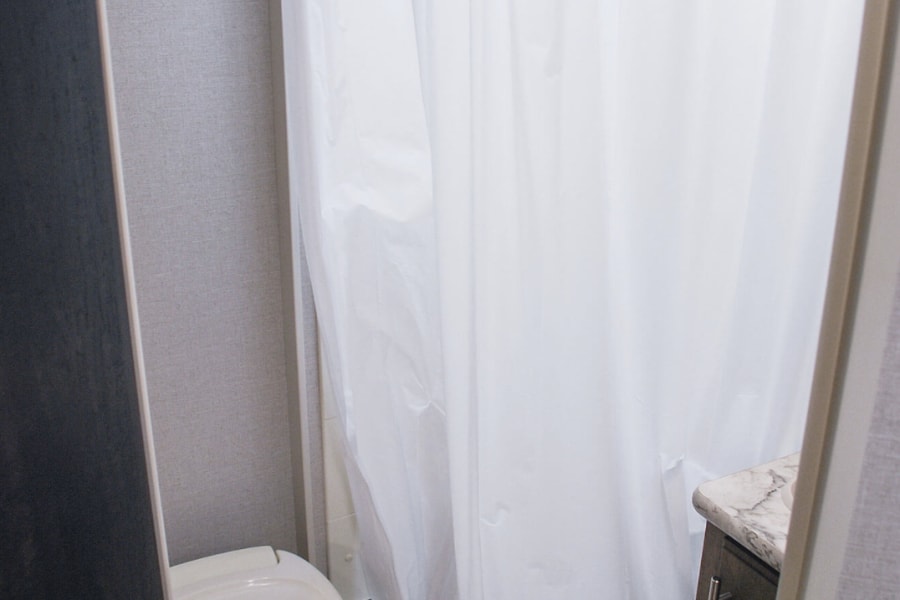 Compact RV rental bathroom: a functional space with a toilet, shower with white curtain, and small vanity.