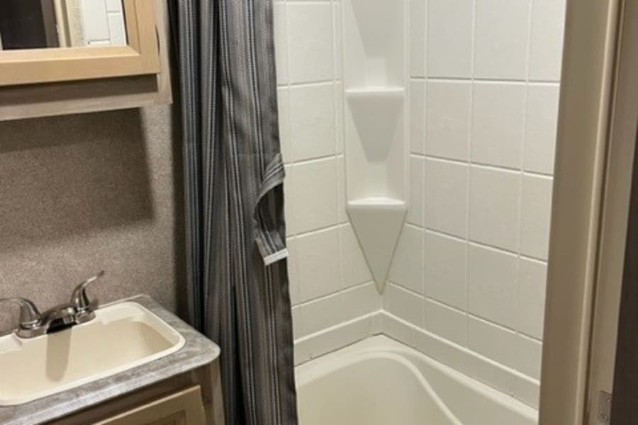 Clean RV rental bathroom with a compact tub/shower, sink, and mirror. Ideal for travel comfort.