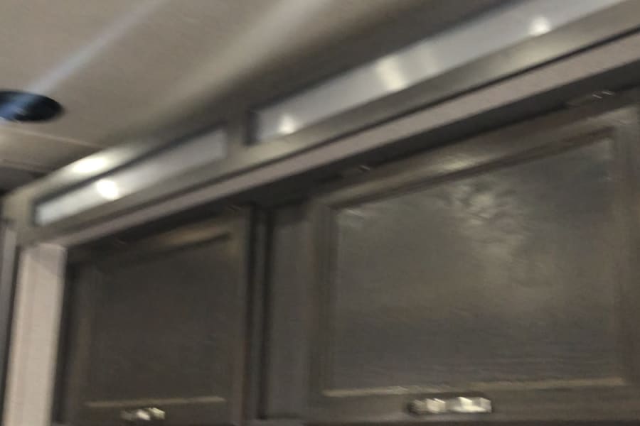 RV rental interior: Overhead cabinets, bright ceiling lights, and a pleated window shade provide comfort and storage.