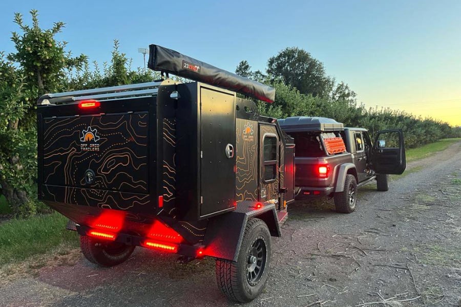 Adventure-ready RV rental: This black off-road camping trailer with topographic graphics is hitched to a Jeep Gladiator truck.