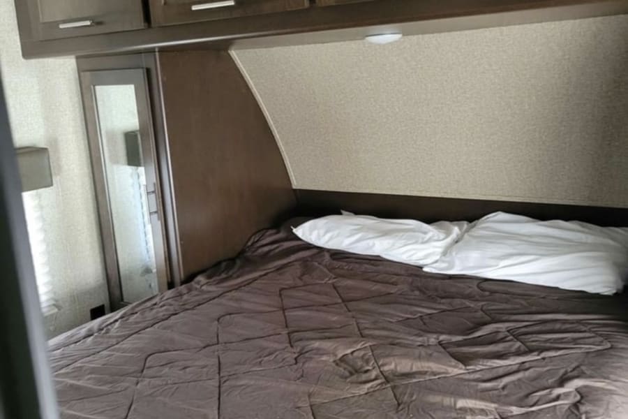 This RV rental bedroom features a bed with a brown comforter, white pillows, and dark wood overhead storage cabinets.