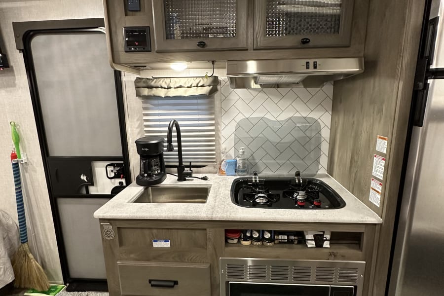 This RV rental features a well-equipped kitchen with a sink, two-burner stovetop, microwave, and overhead storage.