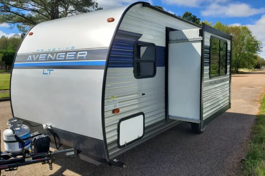 This white and blue Prime Time Avenger LT travel trailer, perfect for an RV rental, shows its extended slide-out.