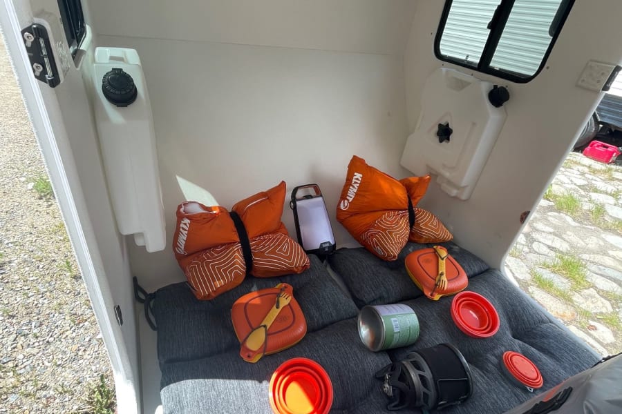 Cozy rv rental interior with a bed setup, water tanks, and essential camping gear for journeys.