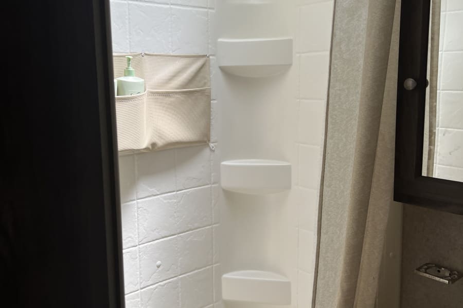 Clean RV rental shower/bathroom with skylight, shower curtain, sink vanity, and hanging organizer. Compact & functional.
