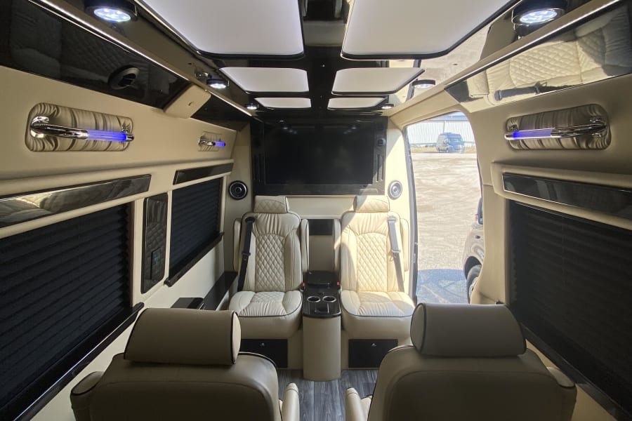 Spacious luxury RV rental interior with individual captain's chairs, large entertainment screen, and ambient lighting.