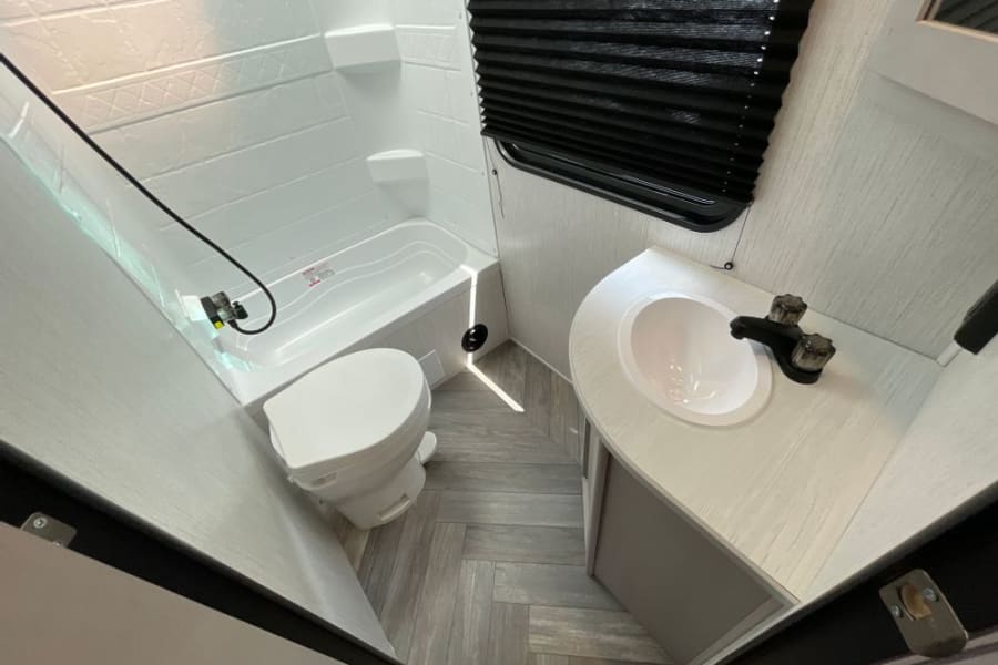 Inside an RV rental, a clean, compact bathroom with a toilet, small tub, and corner sink. Perfect for camper adventures.