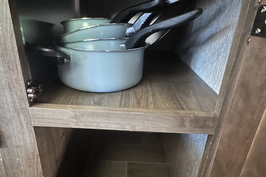 RV rental kitchen cabinet showing stacked light blue cooking pots & empty lower storage space.