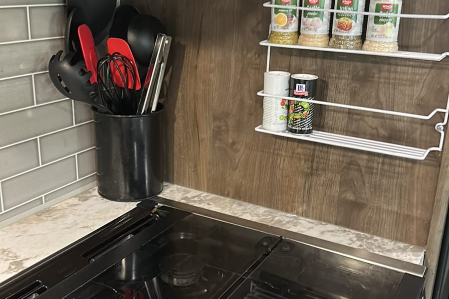 This RV rental kitchenette features a cooktop, mounted spice rack, and utensil holder, perfect for mobile cooking.