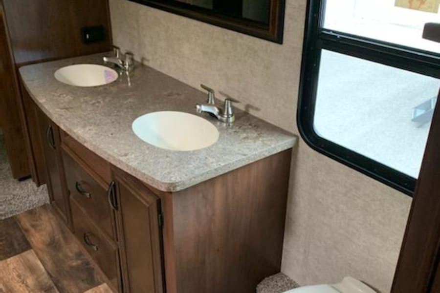 This RV rental bathroom boasts a modern double vanity with two sinks, a toilet, mirror, and wood-look flooring.