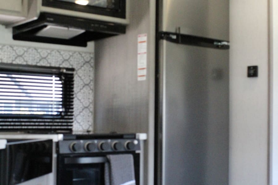 RV rental kitchen featuring a stainless steel refrigerator, microwave, and stove, with light wood-grain cabinets and backsplash.