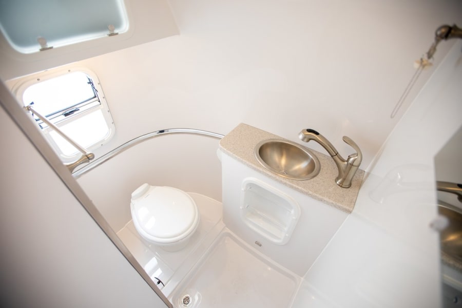 RV rental bathroom: Compact, all-white interior with toilet, sink, and shower area, perfect for adventurers on the go.