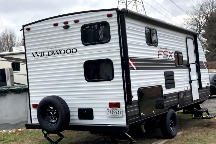 White Forest River Wildwood FSX travel trailer, an rv rental candidate, showing its rear, parked on grass with stabilizers.