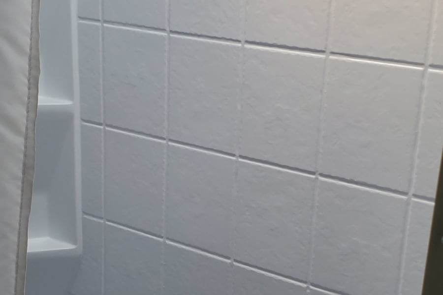 RV rental bathroom: a bright, white shower-tub unit with simulated tile walls and an integrated shelf.