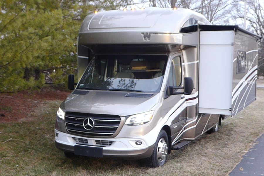 Mercedes-Benz Sprinter motorhome RV rental with an extended slide-out, parked on grass, ready for travel adventures.
