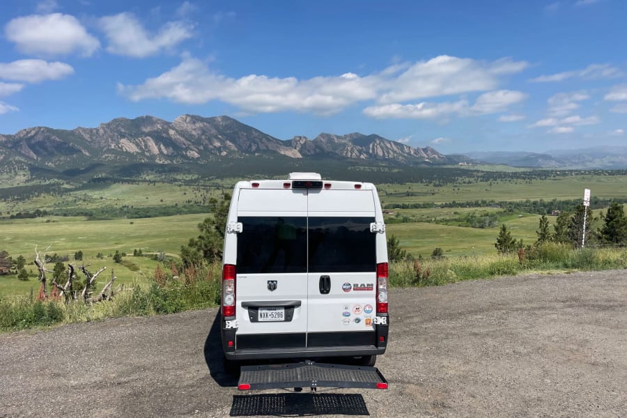 White RV rental van with deployed ramp, framed by majestic mountains and a blue sky. Ideal for accessible adventures.