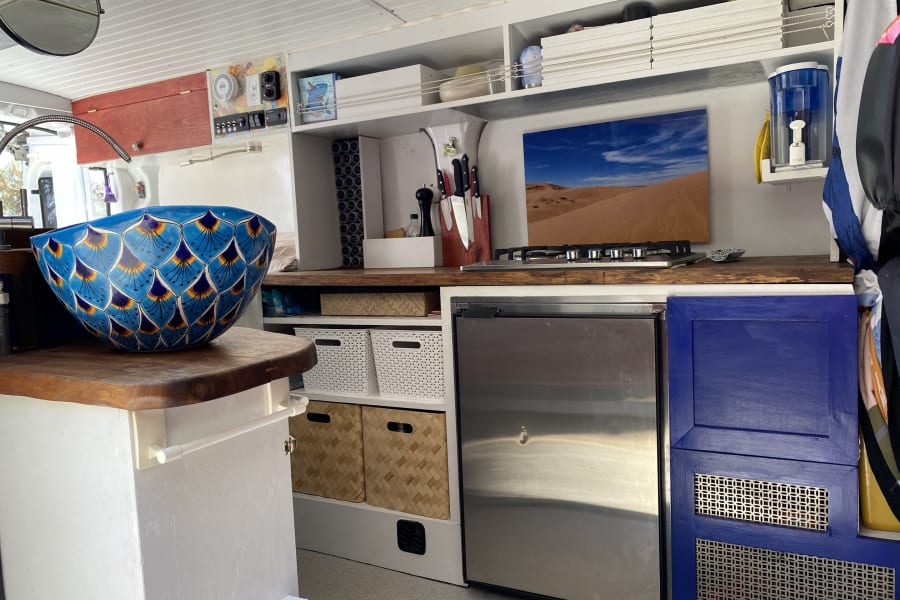 Spacious RV rental kitchen featuring a vibrant blue sink, gas stove, fridge, and ample storage, perfect for your next adventure.