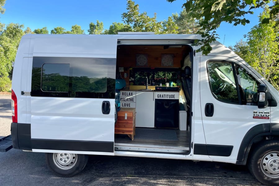 White camper van RV rental with open side door revealing a wood-paneled, minimalist interior. Ideal for van life travel.
