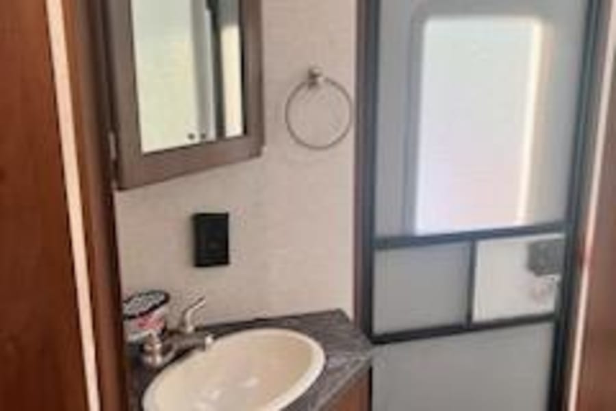This RV rental bathroom features a compact sink, mirror, and functional door. Essential amenities for travel comfort.