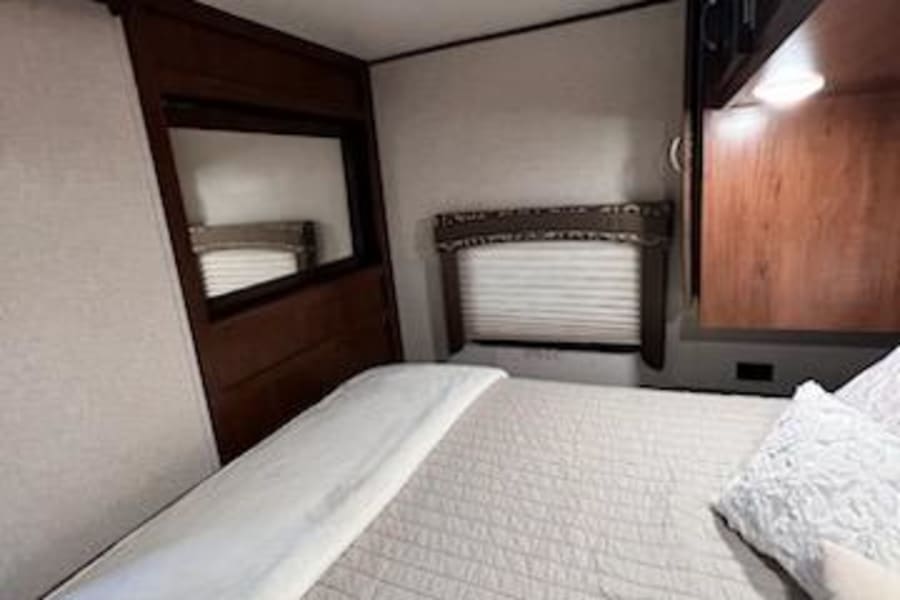 Step inside this cozy RV rental bedroom! Features include a comfy bed, windows with blinds, and rich wood finishes.
