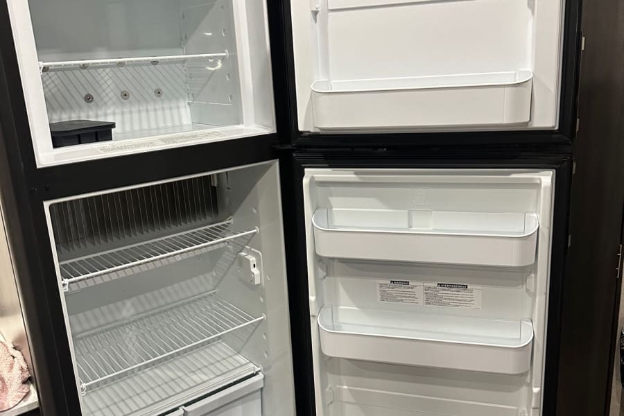 Empty Dometic fridge/freezer inside an RV rental. Wire shelves, door storage, and bins ready for your travel.