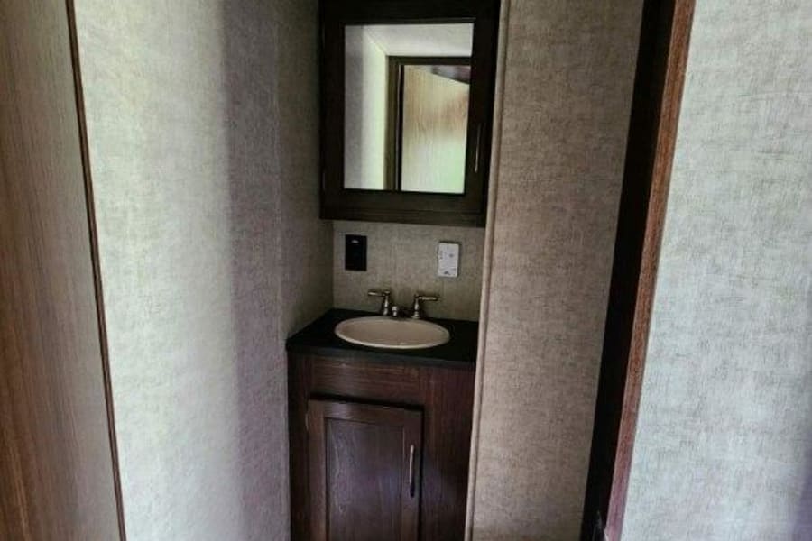 This RV rental's compact bathroom features a white toilet, a practical sink, dark wood vanity with storage, and a mirror.
