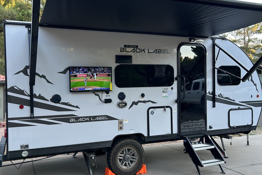 This Wolf Pup Black Label travel trailer RV rental, with an extended awning & outdoor TV, is set up for outdoor fun.