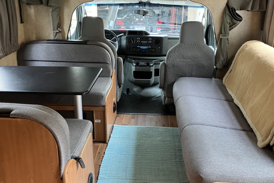 An RV rental's inviting interior, showing the dining area, sofa seating, and the front cockpit from the living space.