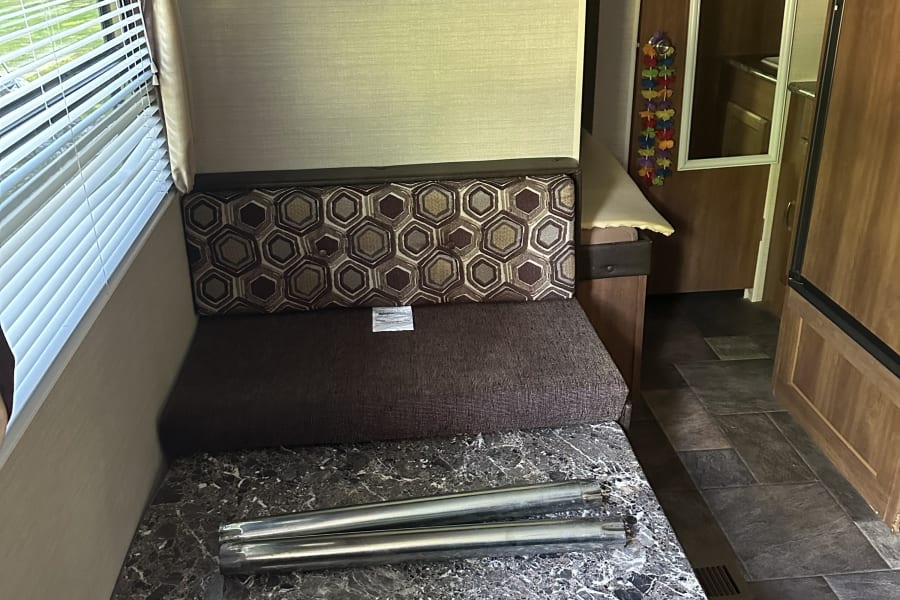 RV rental interior: dinette with patterned bench cushions, window, TV, and table support poles on the tabletop.