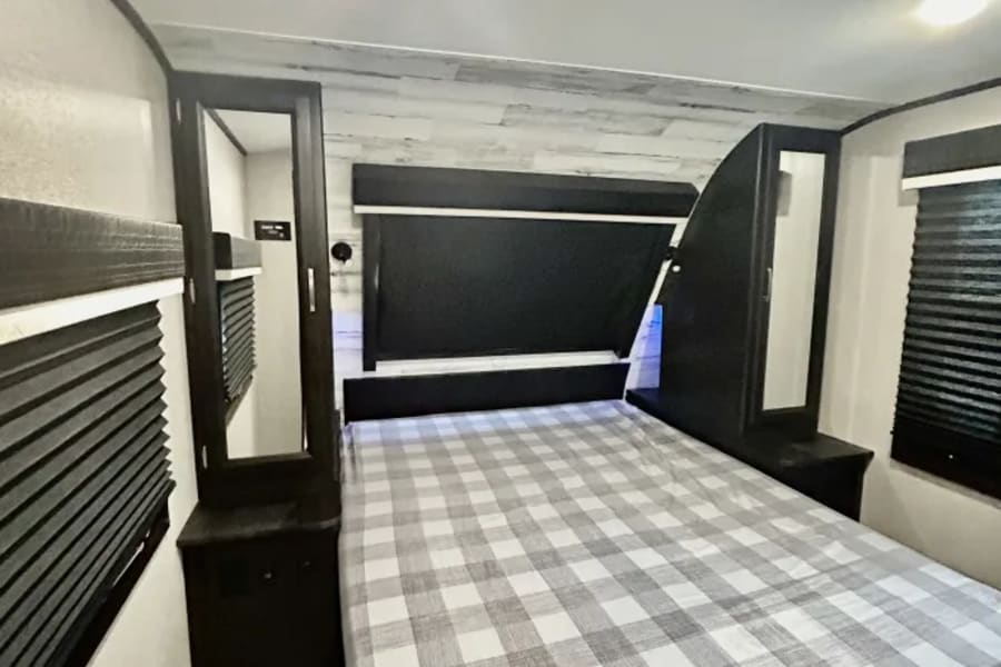 Inside an RV rental: a cozy bedroom with a plaid bed, sleek black headboard, and mirrored cabinets.