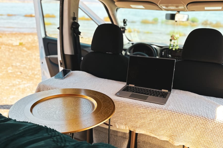 Enjoy remote work from this inviting rv rental. Van interior features a laptop, golden tray, and scenic water view.