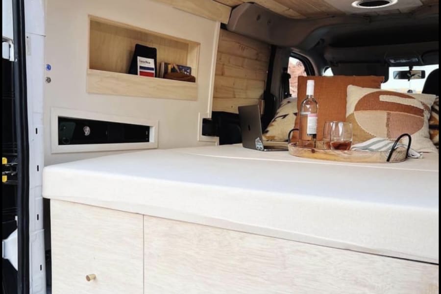 This cozy RV rental features a natural wood ceiling, built-in storage, and a comfy bed. Perfect for van life.