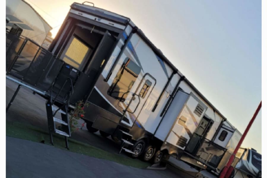 Spacious RV rental with a deployed patio deck, perfect for sunset relaxation. Modern fifth-wheel design.