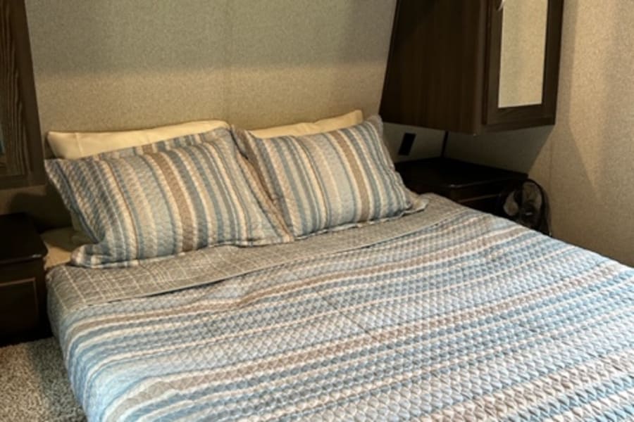 Cozy RV rental bedroom featuring striped bedding, dark wood cabinets, a wall mirror, and ample storage for travelers.