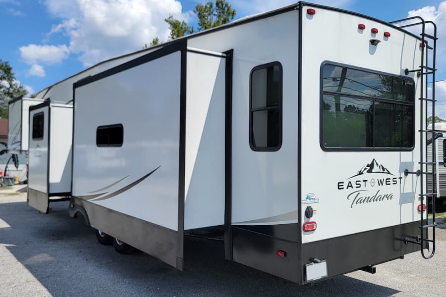 Spacious white East West Tandara RV rental with slide-outs extended, parked outdoors under a blue sky.