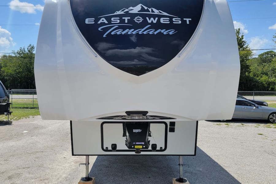 Front view of a white East West Tandara fifth-wheel RV, ideal for an RV rental, parked on a sunny day.