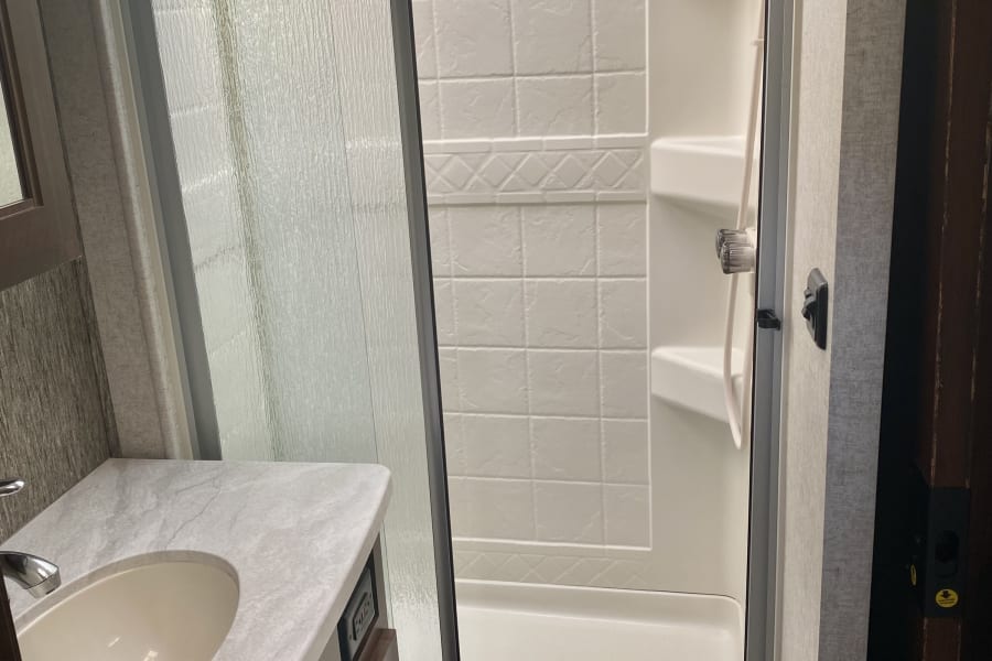 Compact modern RV rental bathroom featuring a bright shower with a textured glass door and a small vanity with sink.