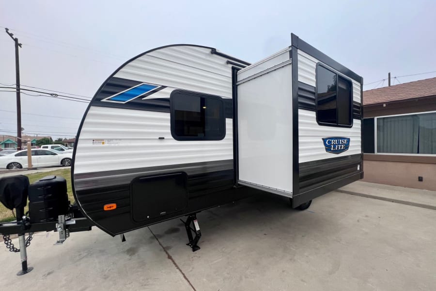 White and black travel trailer for RV rental, featuring an extended slide-out and front hitch assembly.