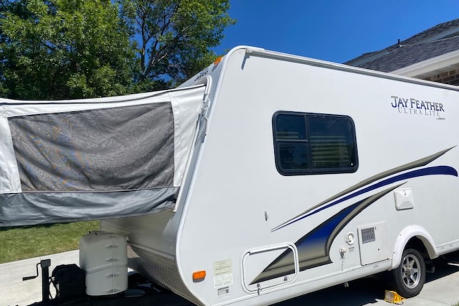 This white Jay Feather Ultra Lite RV rental features blue graphics, a pop-out canvas bunk, and a spare tire, ready for adventure.