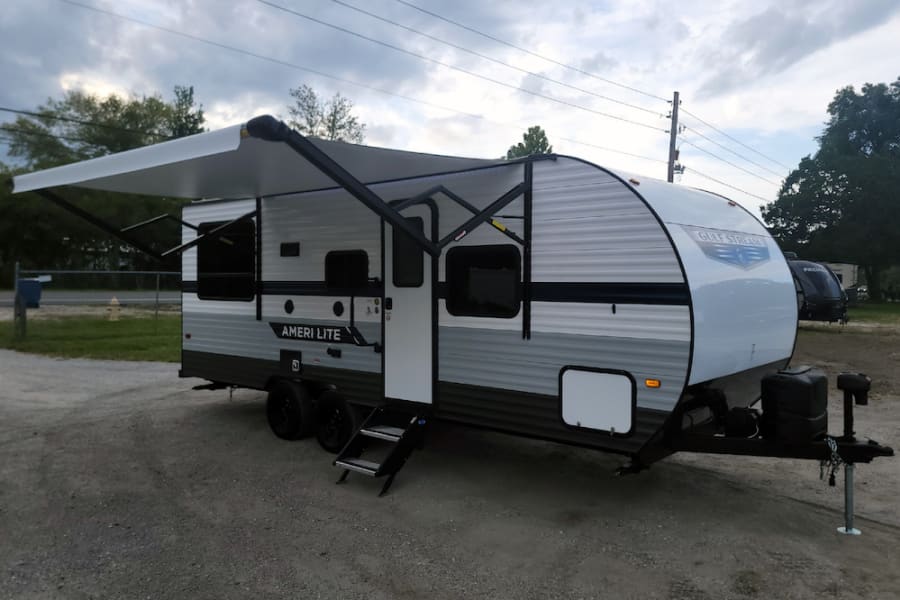 Grey & white Gulf Stream Ameri Lite travel trailer with an extended awning, ready for your RV rental adventure.