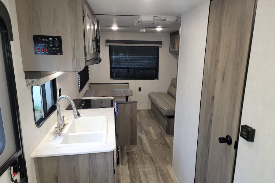 Bright rv rental interior featuring a kitchen with sink, dinette, and sofa. Modern light wood decor and ample living space.