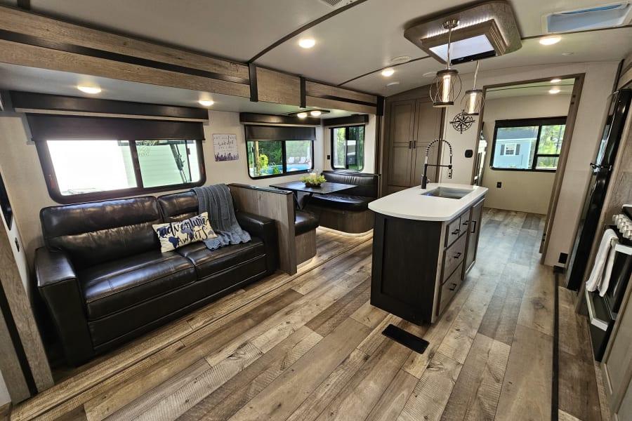 Explore this comfy RV rental interior: spacious living area with a sofa, dining booth, and full kitchen island. Your cozy home on wheels!