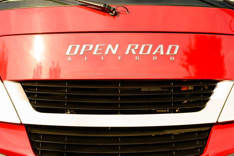 Front of a red 'Open Road Allegro' RV, showing its grille. Ideal for your next rv rental journey.