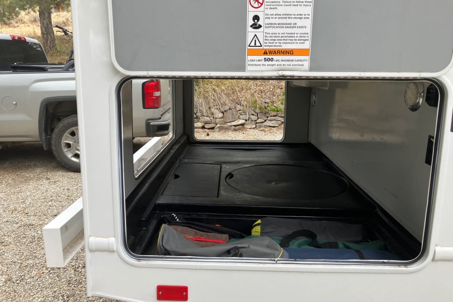 RV rental's spacious pass-through storage bay, loaded with gear, shows important safety warnings.