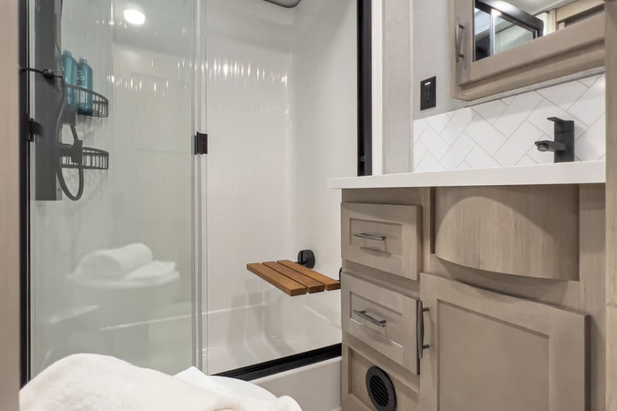 Modern RV rental bathroom: compact with a glass shower, skylight, vanity, and toilet. Bright & functional design.