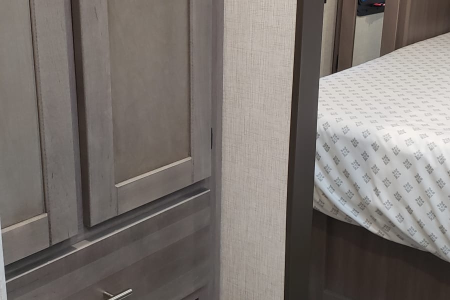 Compact RV rental interior: view of a bathroom with toilet & built-in cabinets, with the bedroom visible beyond.